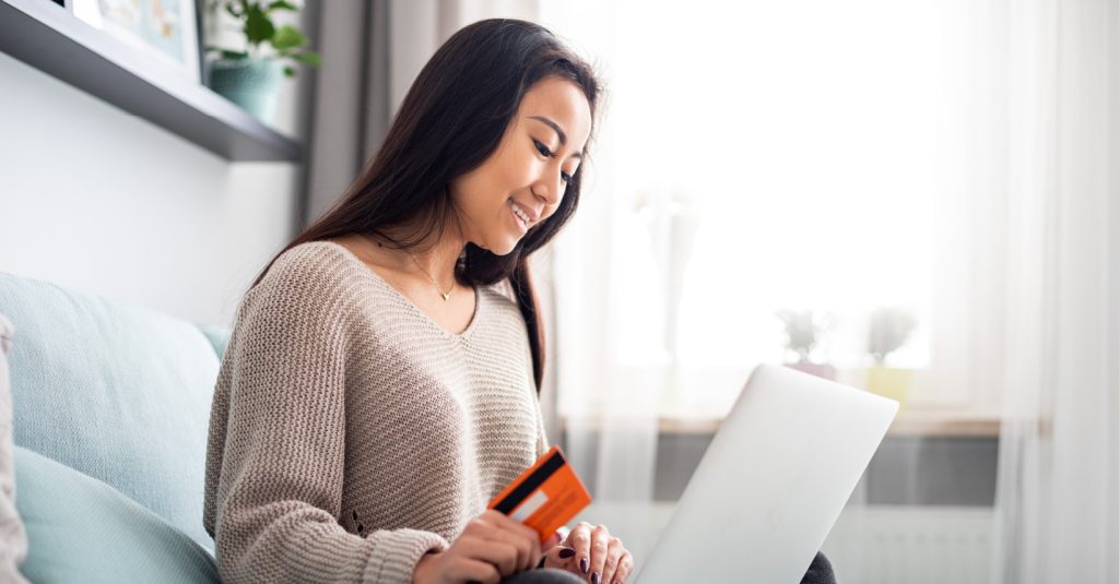 Smiling girl looking at her laptop with her credit card in her hand